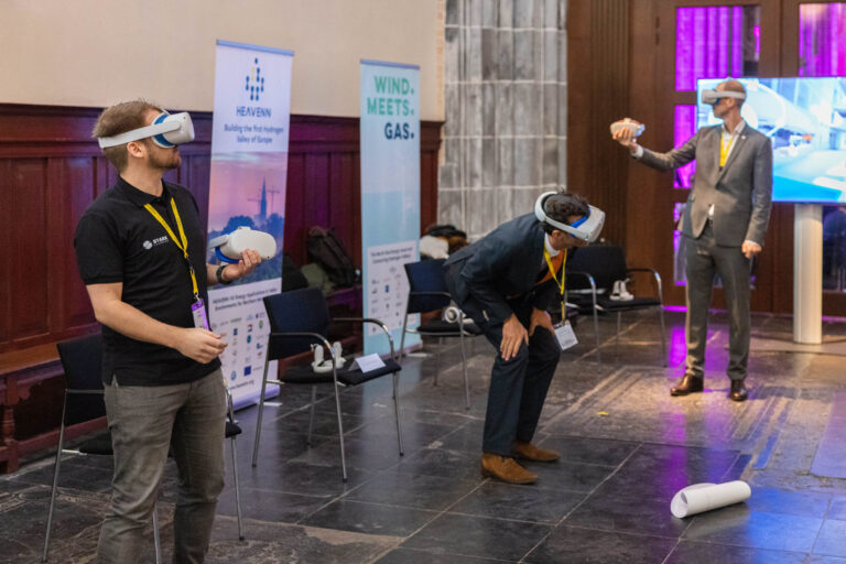 Een groep mensen is bezig met een virtual reality-ervaring in een binnenruimte. Ze dragen VR-headsets en lijken bezig te zijn met een interactieve activiteit. De ruimte heeft een professionele uitstraling met posters over waterstof- en gasprojecten en stoelen gerangschikt in een halve kring. De deelnemers zijn geconcentreerd en bewegen zich binnen hun virtuele omgeving. Deze foto is gemaakt door Jan Buwalda in Groningen.