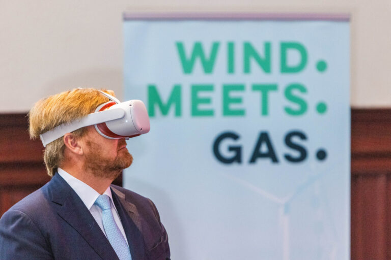 Een persoon in een net pak draagt een virtualreality-bril. Op de achtergrond is een bord te zien met de tekst WIND MEETS GAS. De foto lijkt te zijn genomen tijdens een evenement. Fotograaf: Jan Buwalda, Groningen.