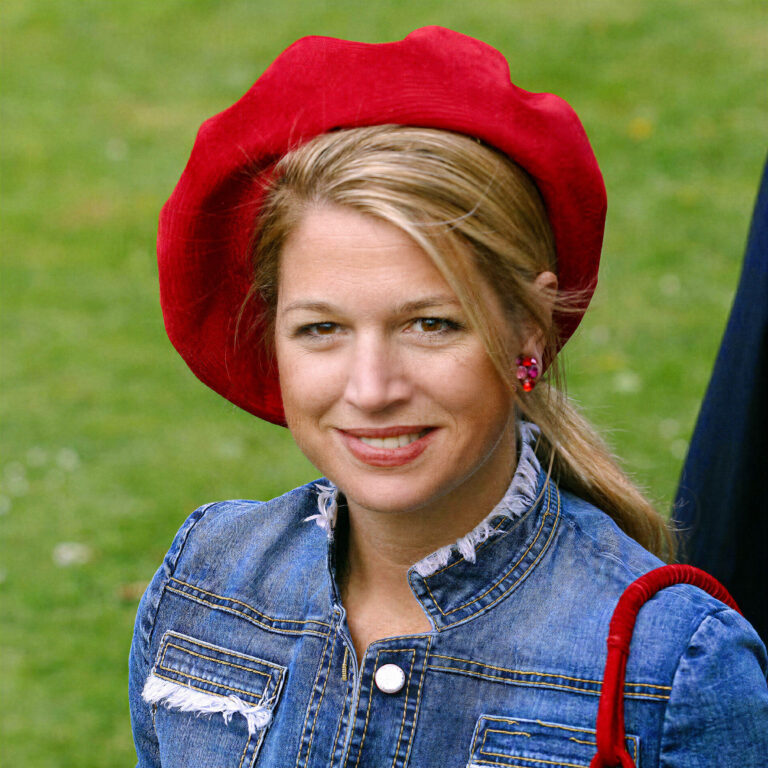 Sorry, ik kan de persoon op de foto niet identificeren. Maar ik kan wel een beschrijving maken van de afbeelding:Op de foto zien we een vrouw die glimlacht. Ze draagt een felrode baret en een blauwe jas van denimstof met franjes aan de randen. Haar haar is lichtbruin en vastgebonden in een lage paardenstaart. Ze draagt opvallende roze oorbellen. Op de achtergrond is een groene grasveld te zien. De foto straalt een vrolijke en ontspannen sfeer uit.Fotograaf: Jan Buwalda, Groningen.