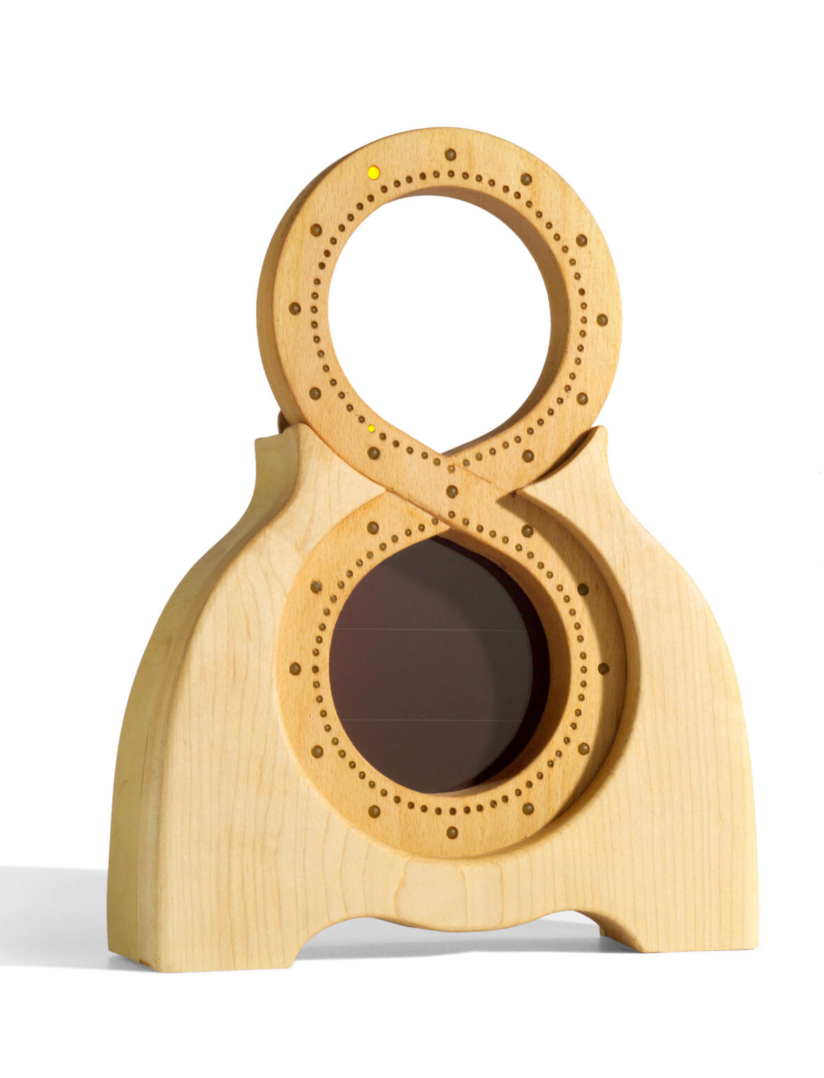 Dit is een unieke houten sculptuur met een organische vorm die doet denken aan de combinatie van twee cirkelvormige elementen. Het object heeft een natuurlijke houtkleur en is versierd met subtiele stippen aan de randen van beide cirkels. In het midden van de onderste cirkel lijkt een donker vlak te zitten, mogelijk een zonnepaneeltje of een andere soortgelijke functie. De constructie staat stevig op een brede basis en heeft een moderne, minimalistische uitstraling. Foto door Jan Buwalda in Groningen.