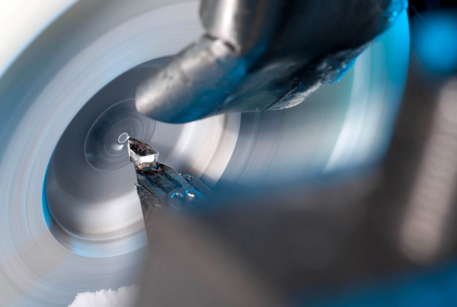 De foto toont een close-up van een draaibankproces, waarbij een metaalstuk wordt bewerkt. De draaischijf draait met hoge snelheid, wat te zien is aan de bewegingsonscherpte. Het metaal wordt nauwkeurig gesneden door een scherpe snijkop. De combinatie van blauwige tinten en het zilverkleurige metaal zorgt voor een industriële sfeer. Foto door Jan Buwalda in Groningen.
