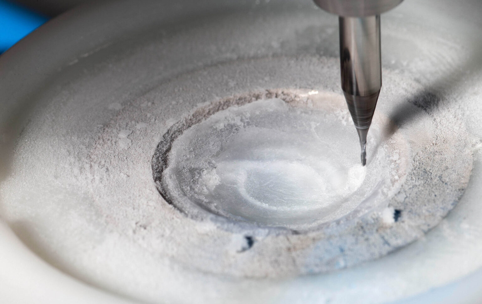 Dit is een close-up foto van een machine die werkt met ijs of een koude substantie, mogelijk in een laboratoriumomgeving. De foto toont een nauwkeurige bewerking met een metalen gereedschap dat in contact is met een rond oppervlak bedekt met frost. De aandacht voor detail in de texturen en de focus op het gereedschap creëren een fascinerend beeld van precisiewerk. Foto door Jan Buwalda uit Groningen.