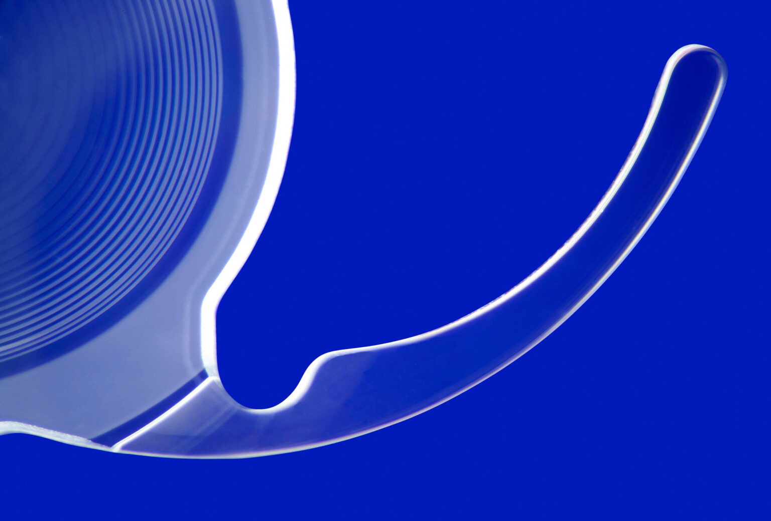 Een abstracte foto toont een doorschijnende en licht gebogen vorm tegen een heldere, blauwe achtergrond. De fijne ringen en lijnen suggereren een gevoel van beweging en diepte. De eenvoud en de contrasterende kleuren geven het geheel een moderne uitstraling. Fotograaf: Jan Buwalda, Groningen.