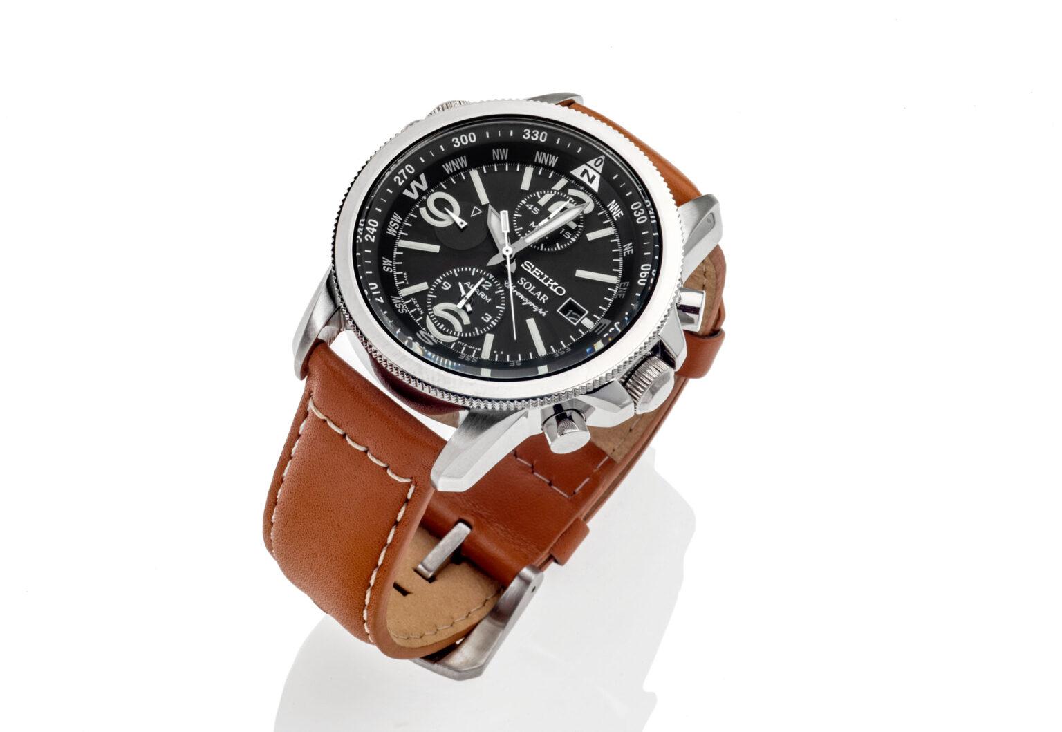 Dit is een foto van een stijlvolle Seiko Solar chronograaf. Het horloge heeft een robuuste zilveren kast en een bruine leren band, wat een klassieke uitstraling geeft. De wijzerplaat is zwart met verschillende subdials en markeringen rondom. De foto is gemaakt tegen een witte achtergrond, waardoor het horloge volledig tot zijn recht komt. Fotograaf: Jan Buwalda, Groningen.