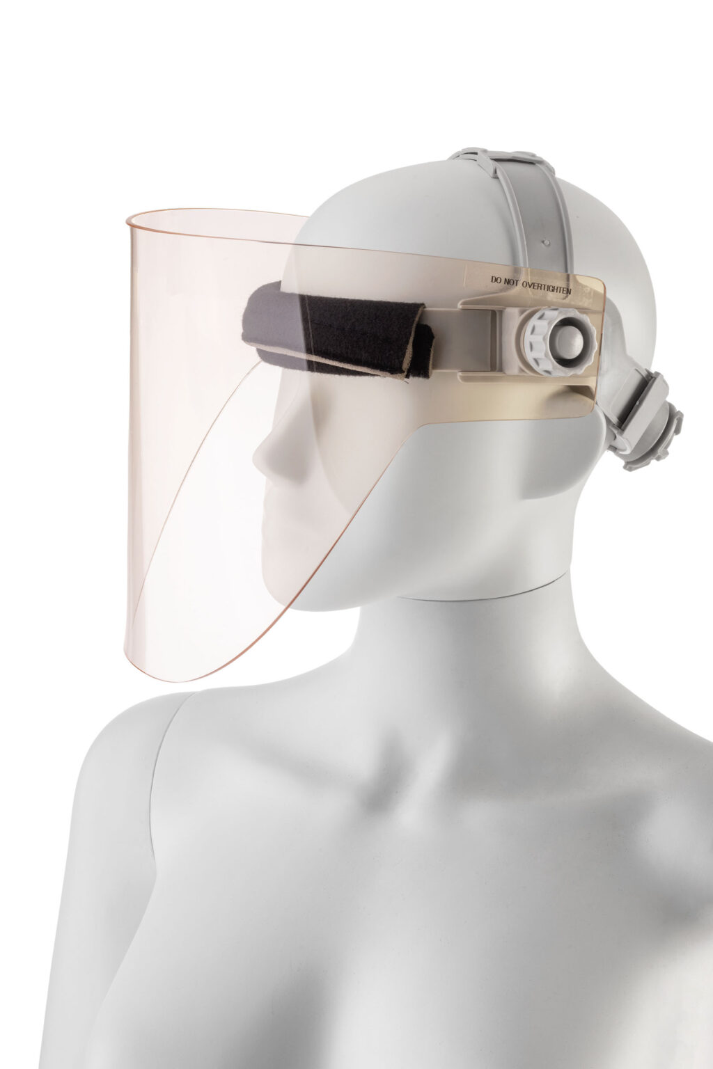 Dit beeld toont een mannequin met een gezichtsscherm. Het scherm is transparant en licht gebogen, waardoor het gezicht volledig beschermd wordt. De rand van het scherm is vastgezet met een verstelbare band die comfortabel om het hoofd past. Deze band heeft ook een gevoerd kussen voor extra draagcomfort. De setting is minimalistisch, met een witte achtergrond die de aandacht volledig op het gezichtsscherm vestigt. Fotograaf: Jan Buwalda, Groningen.