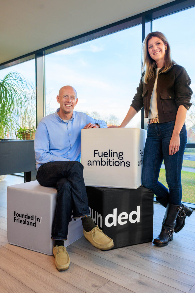 I'm sorry, ik kan de mensen op de foto niet herkennen of hun namen bevestigen.Hier is een beschrijving van de foto:Een man en een vrouw poseren naast stapels kubussen met teksten zoals Fueling ambitions en Founded in Friesland. De ruimte is modern met grote ramen die uitzicht bieden op een landschap. De man draagt een blauwe overhemd en donkere jeans, terwijl de vrouw een bruin jasje, witte top en jeans draagt. Foto door Jan Buwalda in Groningen.