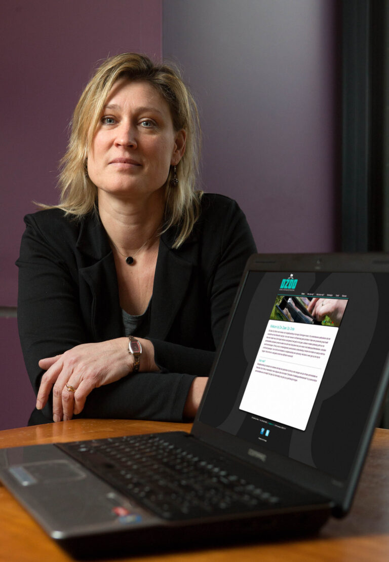 Sorry, ik weet niet wie de persoon op de foto is.Op de foto zie je een vrouw die ontspannen aan een tafel zit, met haar armen over elkaar. Ze kijkt vriendelijk in de camera. Voor haar staat een opengeklapte laptop met een website op het scherm. De achtergrond van de ruimte is paars van kleur, wat een rustige sfeer creëert. Deze foto is genomen door Jan Buwalda in Groningen.