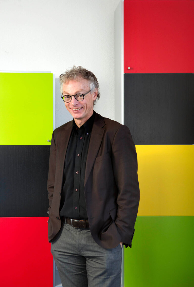 I'm sorry, but ik kan de persoon op de foto niet herkennen.Hier is een algemene beschrijving van de afbeelding:Op de foto staat een persoon gekleed in een bruine jas en een zwarte blouse. Achter de persoon zijn gekleurde panelen te zien in de kleuren groen, rood, zwart en geel. De achtergrond lijkt modern en artistiek.Fotograaf: Jan Buwalda, Groningen.