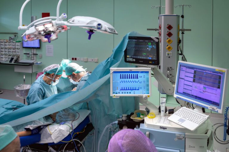 Dit beeld toont een operatiekamer waarin een team van medisch specialisten geconcentreerd werkt aan een chirurgische ingreep. De kamer is uitgerust met moderne medische apparatuur, waaronder monitors voor vitale functies en operatieverlichting. De zorgvuldigheid waarmee de artsen te werk gaan, is zichtbaar in hun focus en samenwerking. De foto is genomen door Jan Buwalda in Groningen.