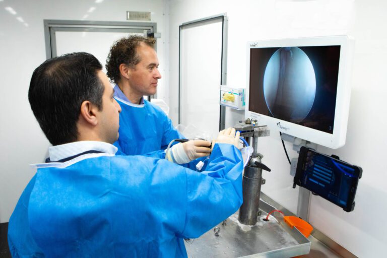 Twee mannen in medische kleding werken samen in een laboratoriumsetting. Ze bekijken een scherm waarop een afbeelding vanbinnen wordt getoond. De focus ligt op precisie bij het gebruik van instrumenten. Fotograaf: Jan Buwalda, Groningen.