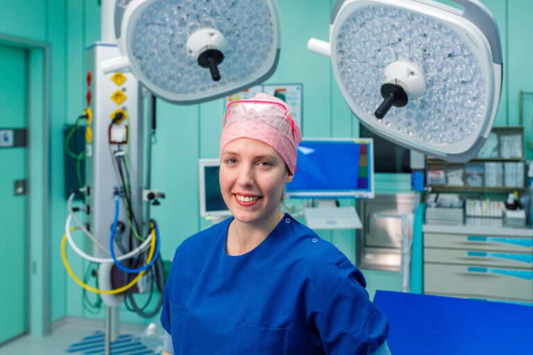 Ik ben sorry, ik weet niet wie deze persoon is.Beschrijving: De afbeelding toont een persoon in een operatiekamer. Ze draagt blauwe medische kleding en een roze operatiehoed. De omgeving is uitgerust met medische apparatuur, zoals chirurgische lampen en monitoren. De algehele sfeer is professioneel en klinisch.Fotograaf: Jan Buwalda, Groningen.